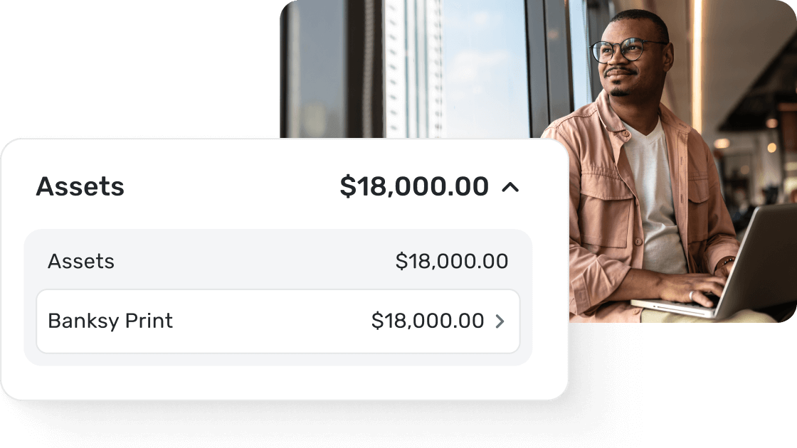 Man working on laptop with Quicken Simplifi assets screen displaying total assets of $18,000, including manually tracked Banksy Print