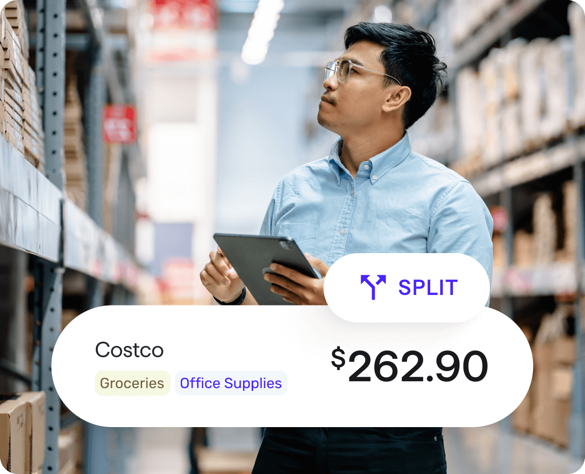 A person wearing glasses stands in a warehouse aisle holding a tablet and looking at shelves stocked with boxes. Overlaid on the image is a transaction card showing ‘Costco,’ category labels ‘Groceries’ and ‘Office Supplies,’ a ‘Split’ icon, and a total amount of $262.90.
